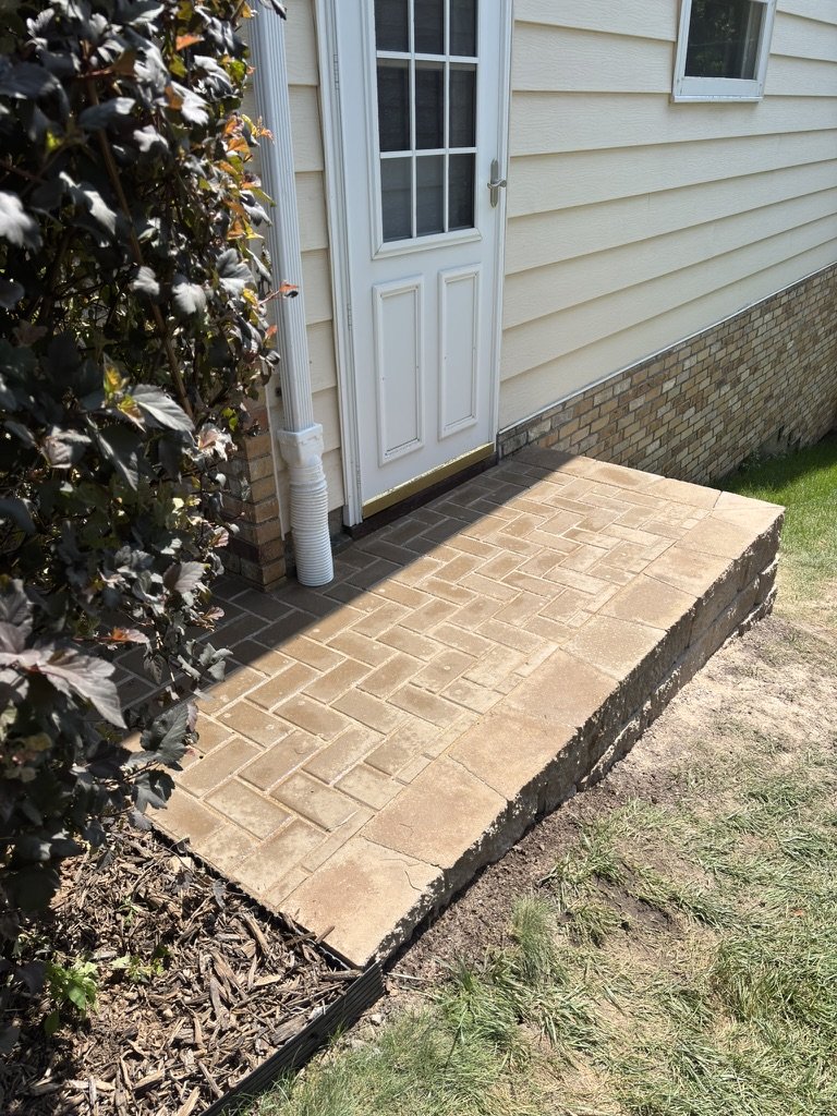 Finished herringbone paver patio at the side door, level with the top of the retaining wall