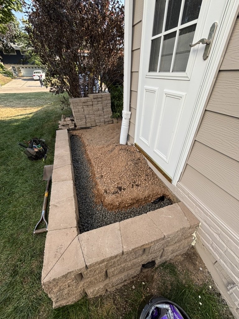 Retaining wall under construction with gravel base trench and stacked pavers ready for installation